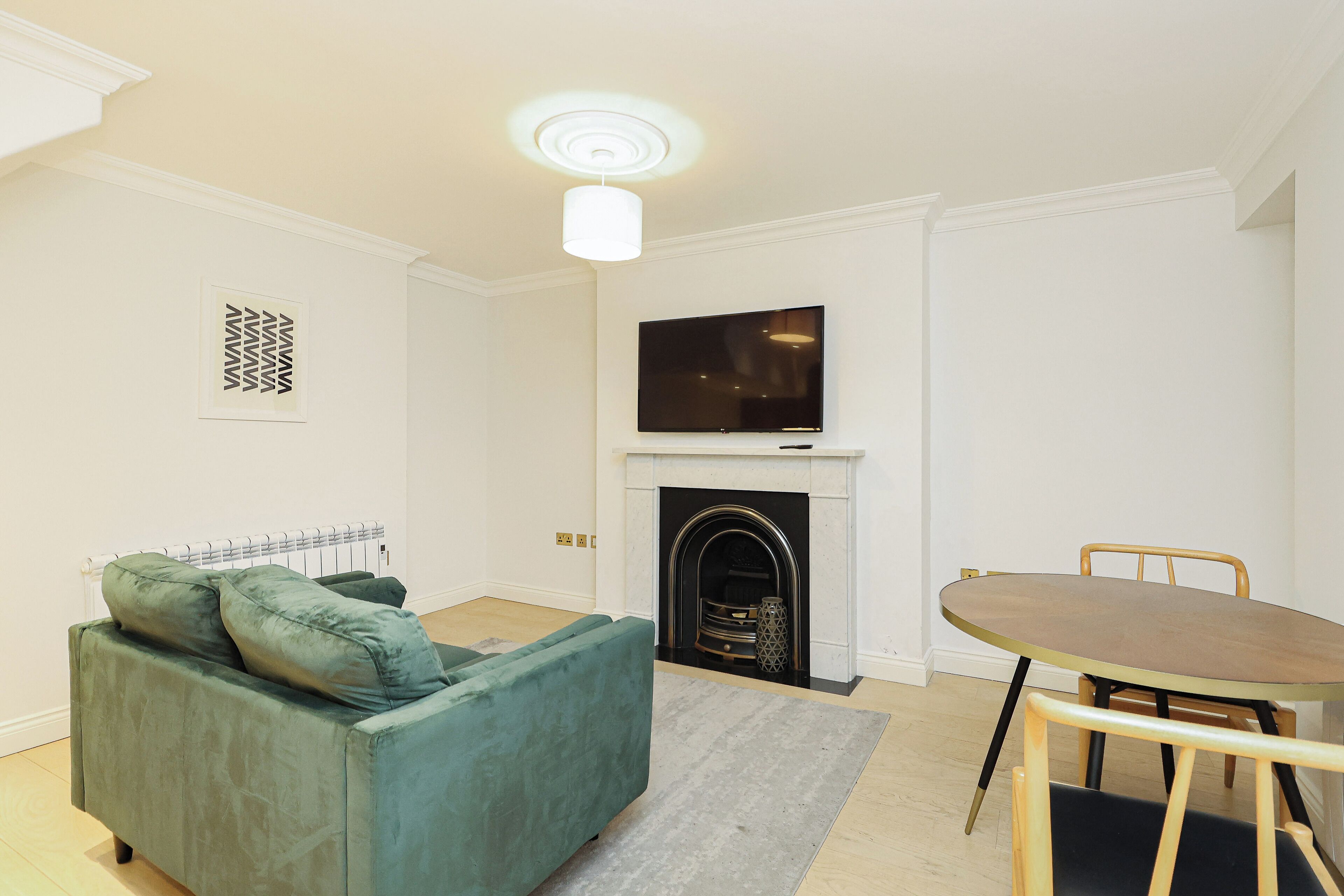 A living room with a green sofa, a fireplace, a television, and a dining table.