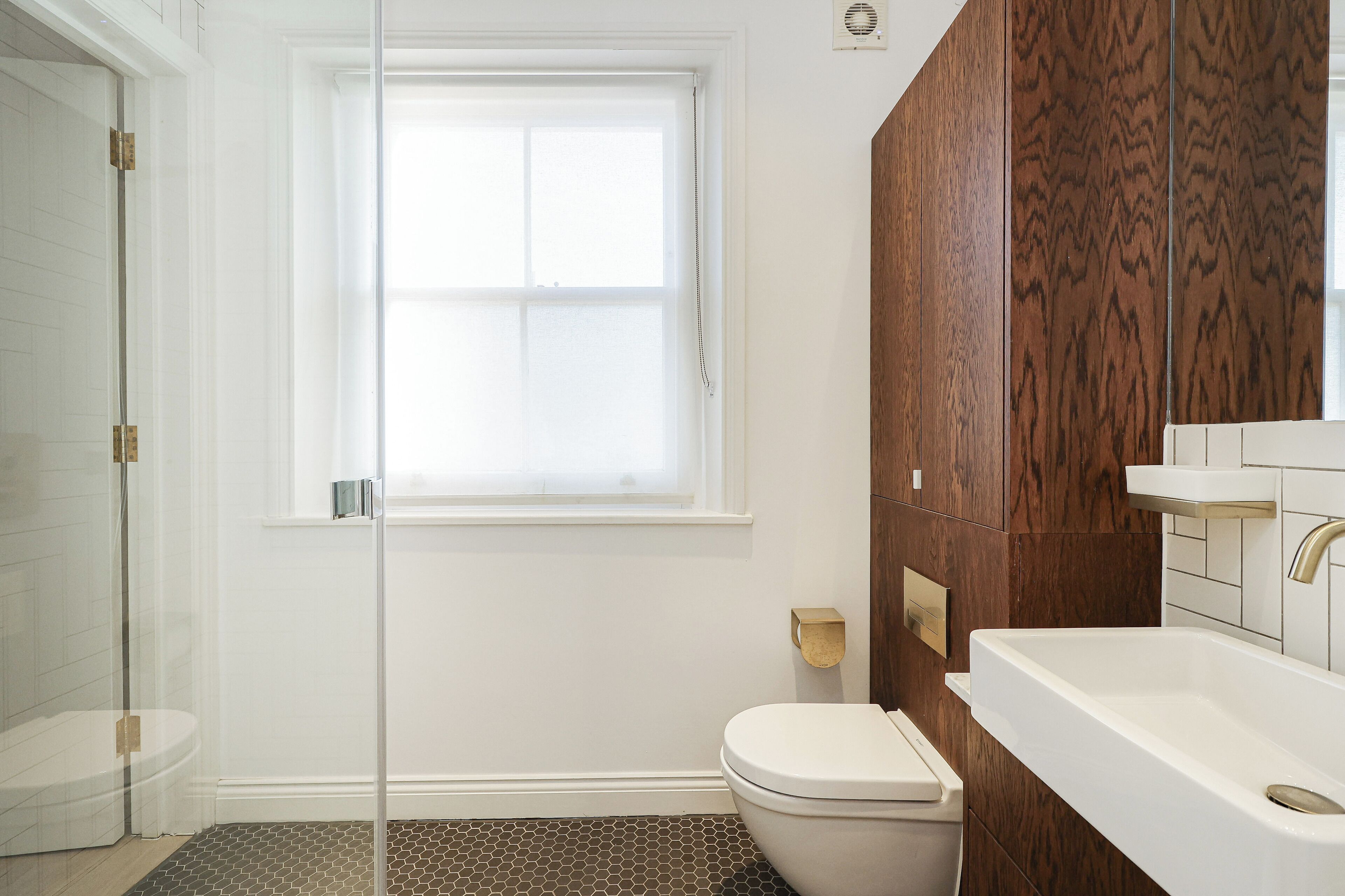 A bathroom with a glass shower door, a toilet, a sink, and a window.