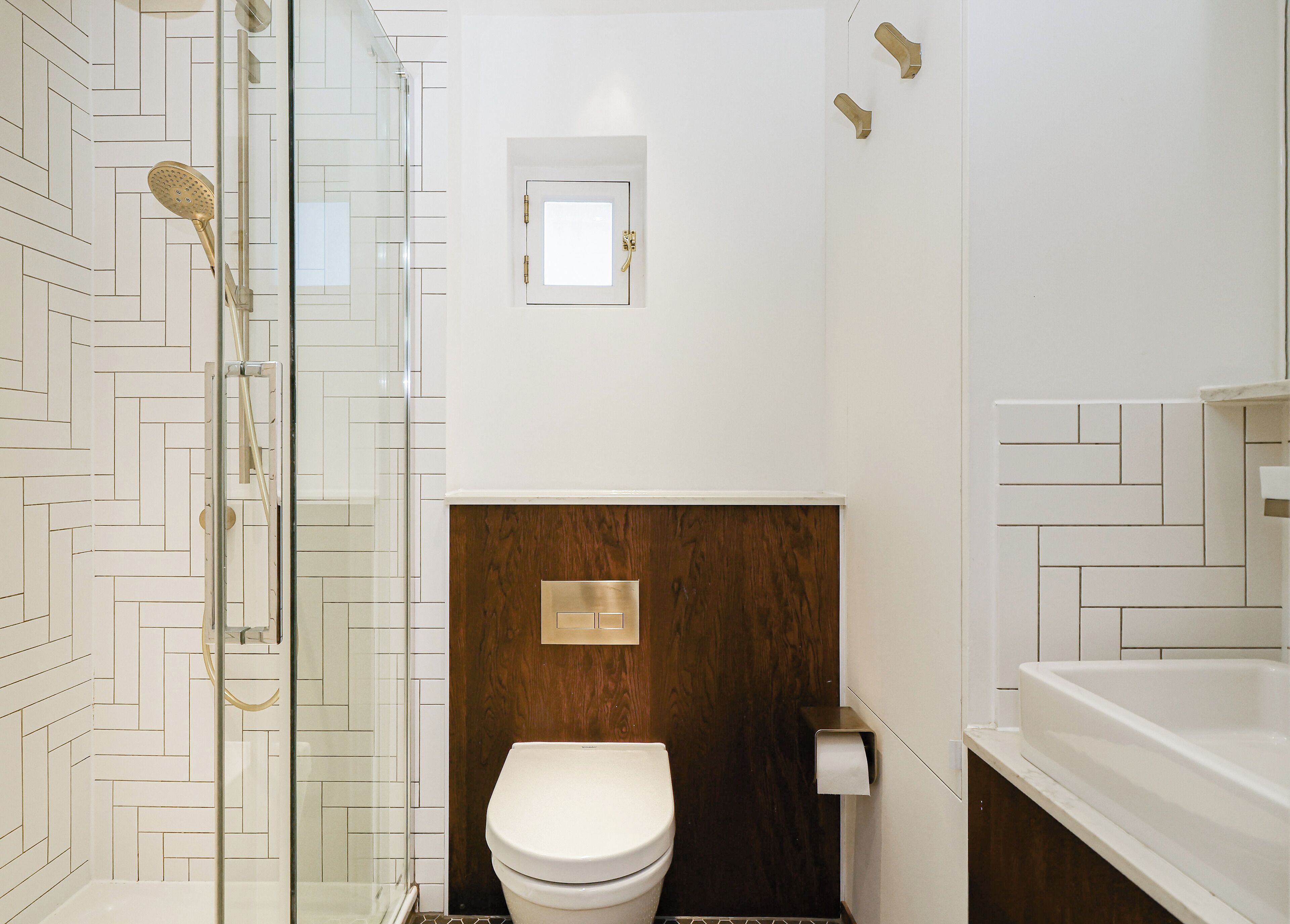 A modern bathroom with a glass shower enclosure, a wooden vanity, and a white toilet.