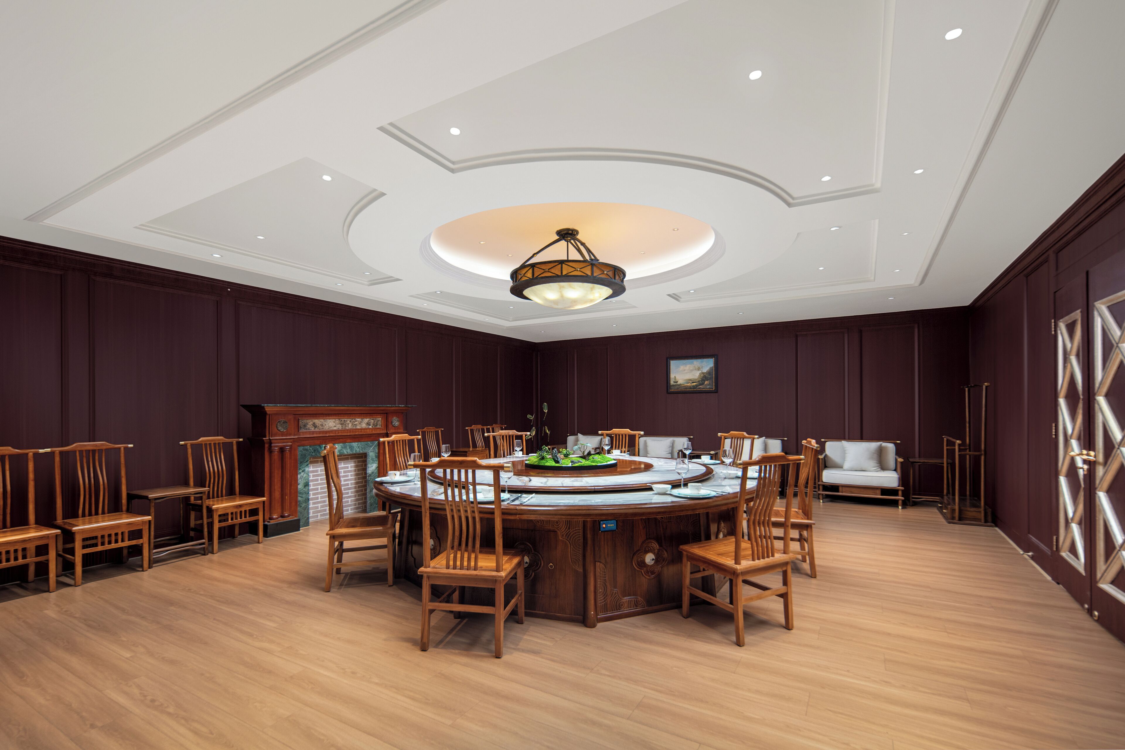 Uma mesa de jantar redonda cercada por cadeiras de madeira em um quarto com paredes de madeira escura e teto branco com iluminação embutida.
