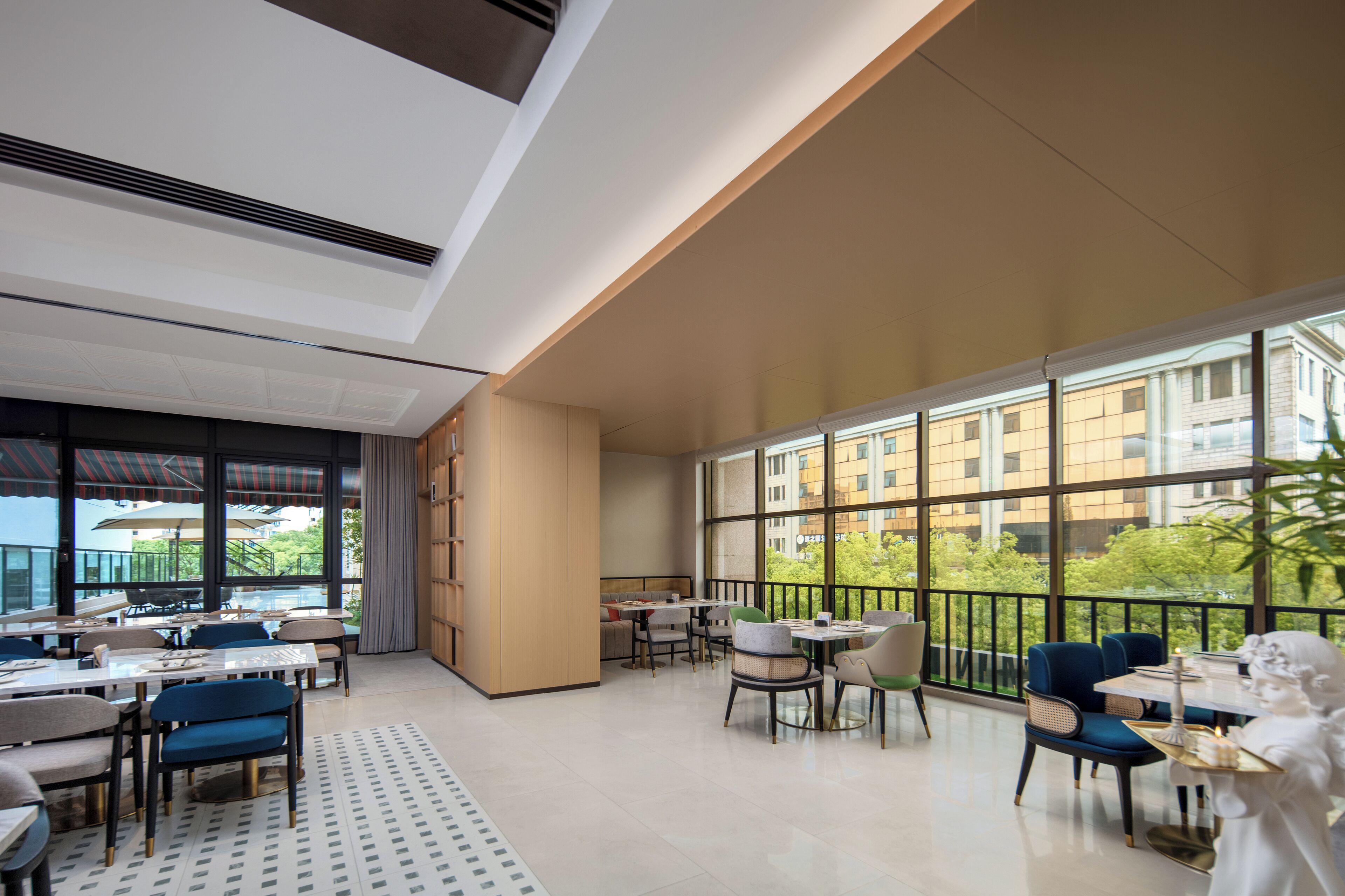 A spacious indoor area with multiple tables and chairs, large windows offering views of buildings and trees, and a statue on a table.