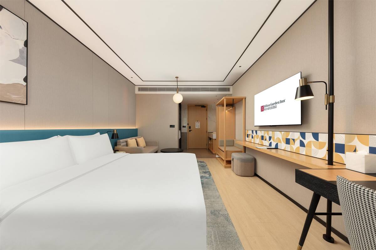 A hotel room with a bed, a desk, a chair, a TV, and a lamp.