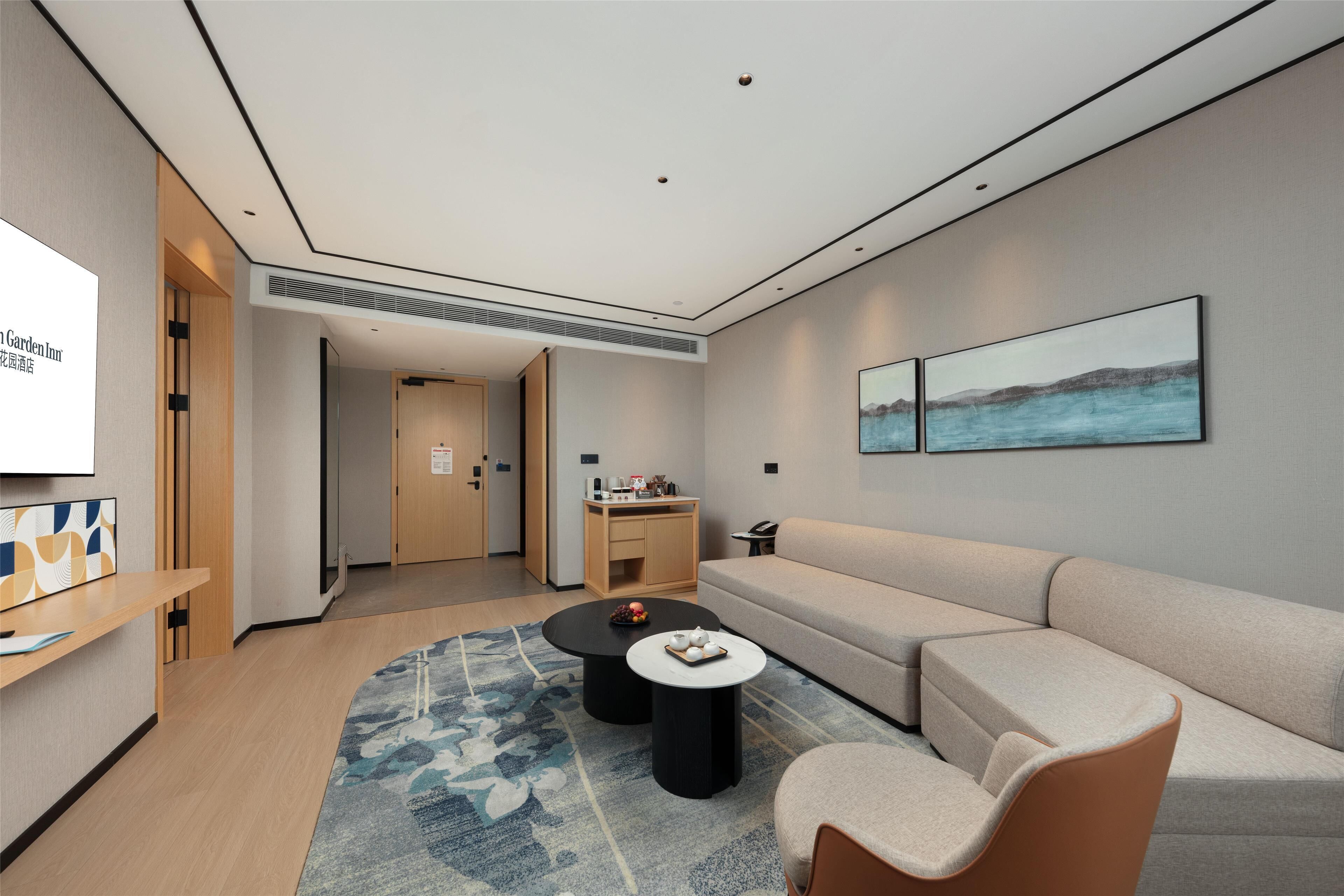 A modern hotel room with a sofa, a coffee table, a TV, and a painting on the wall.