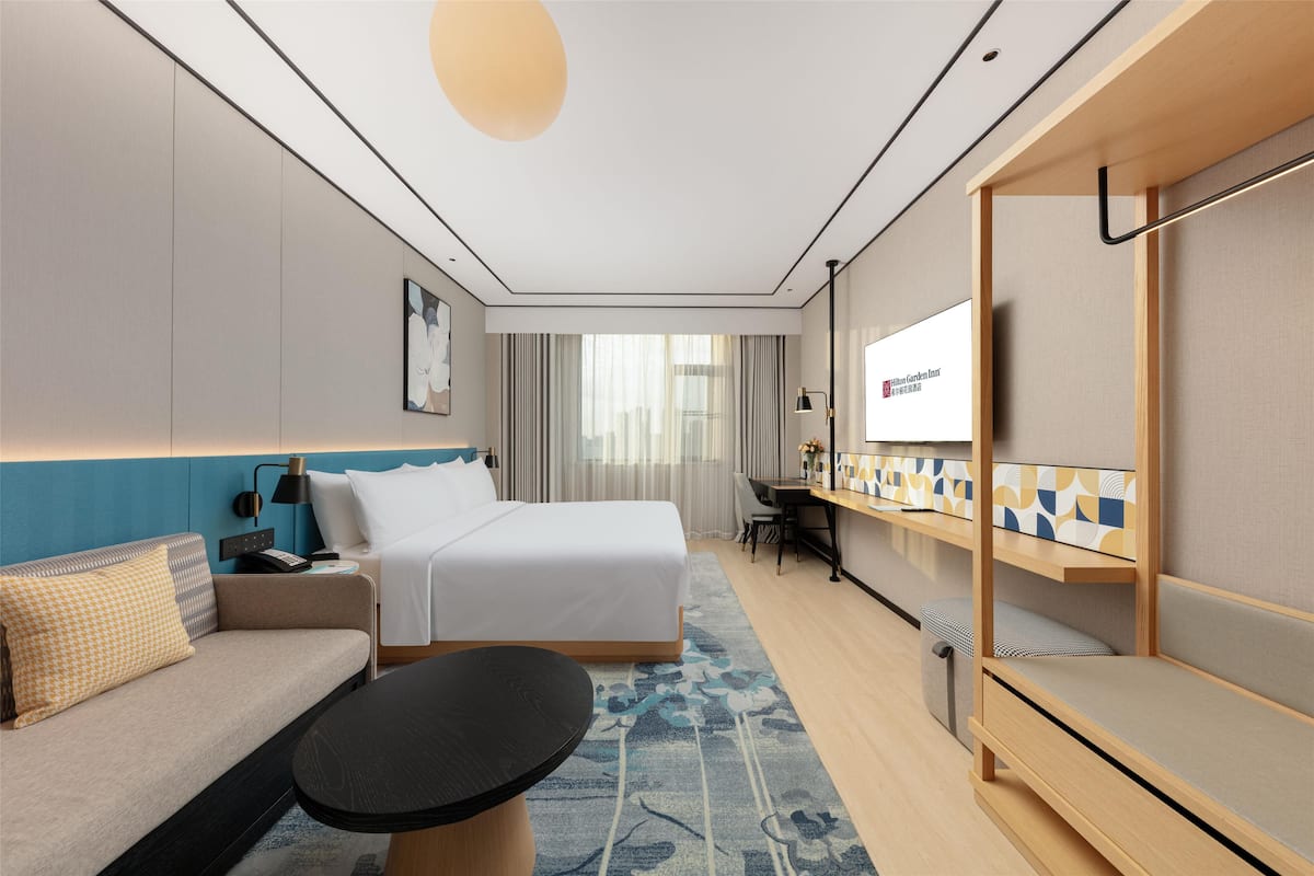 A hotel room with a bed, a sofa, a desk, and a TV.