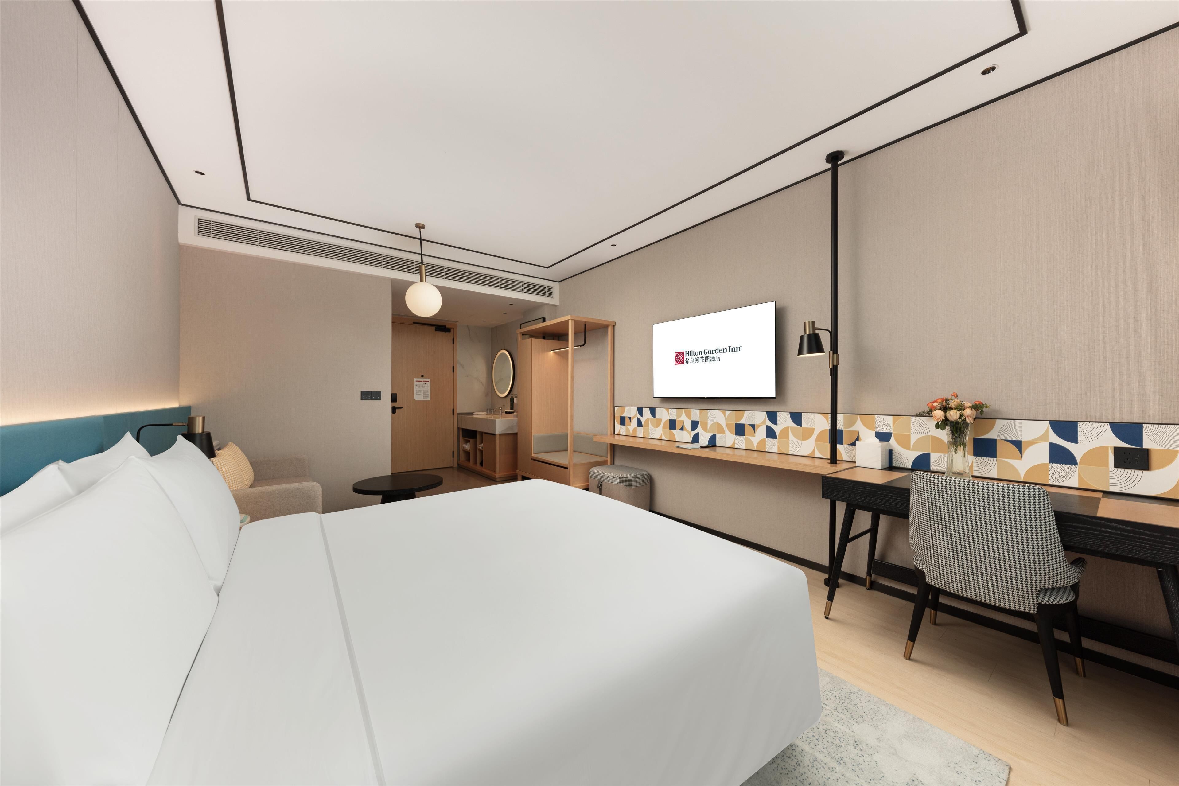 A hotel room with a bed, a desk, a chair, a TV, and a bathroom.