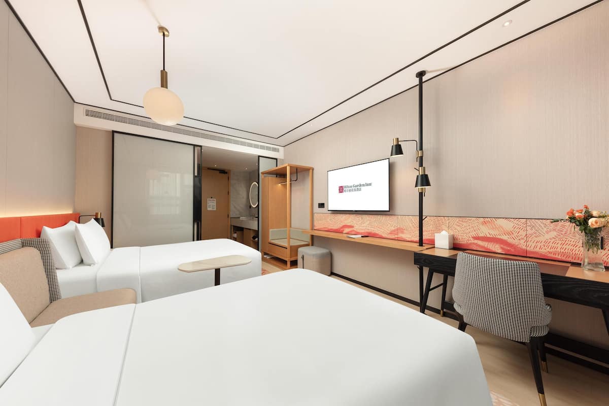 A modern hotel room with a bed, a desk, and a TV displaying the hotel name.