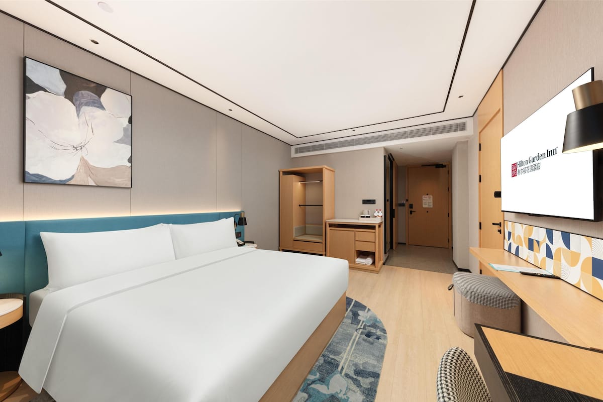 A hotel room with a large bed, a desk, a chair, a wardrobe, and a television.