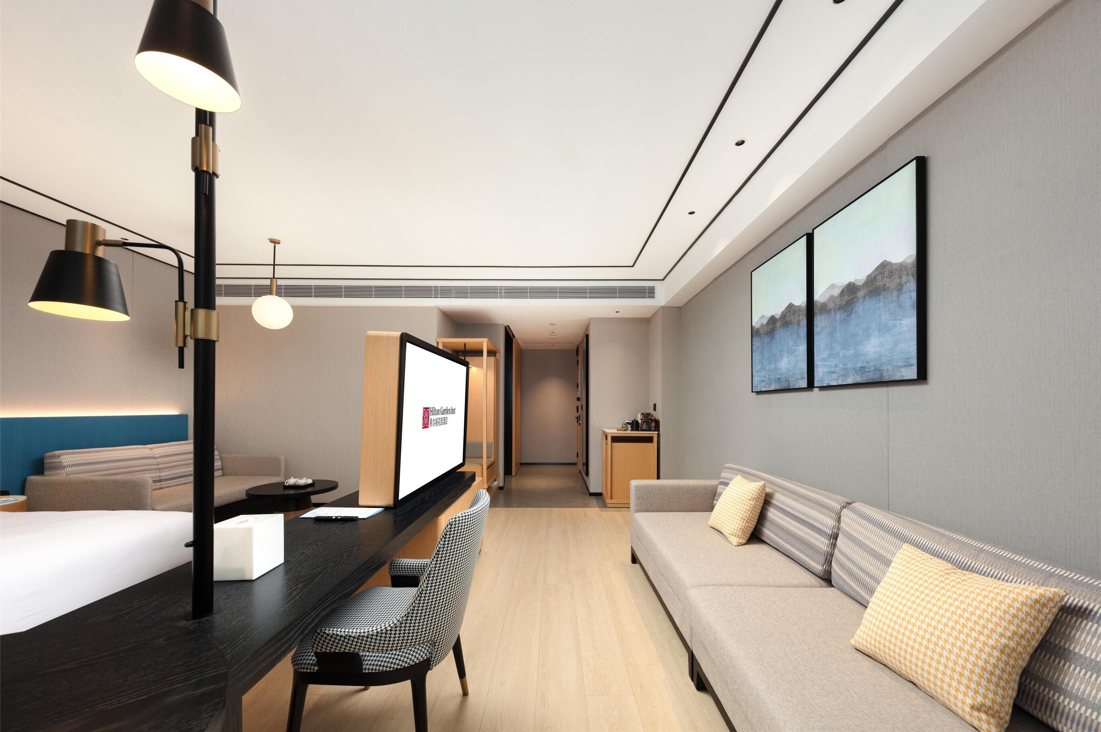 Habitació d'hotel moderna amb llit, escriptori, cadira, sofà i televisió.