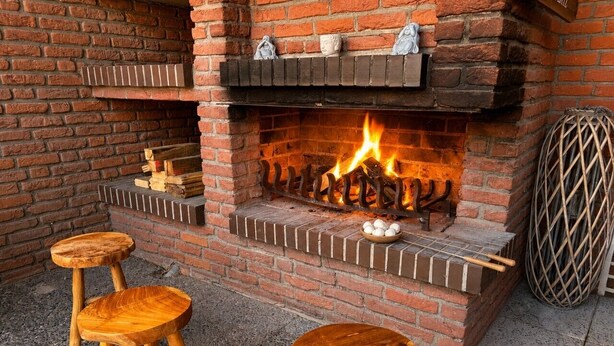 Ein Kamin aus Ziegelsteinen mit Feuer, zwei hölzerne Hocker und ein Korb Eier.