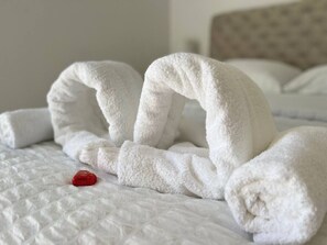 A neatly made bed with white linens and a single red object on the bed.
