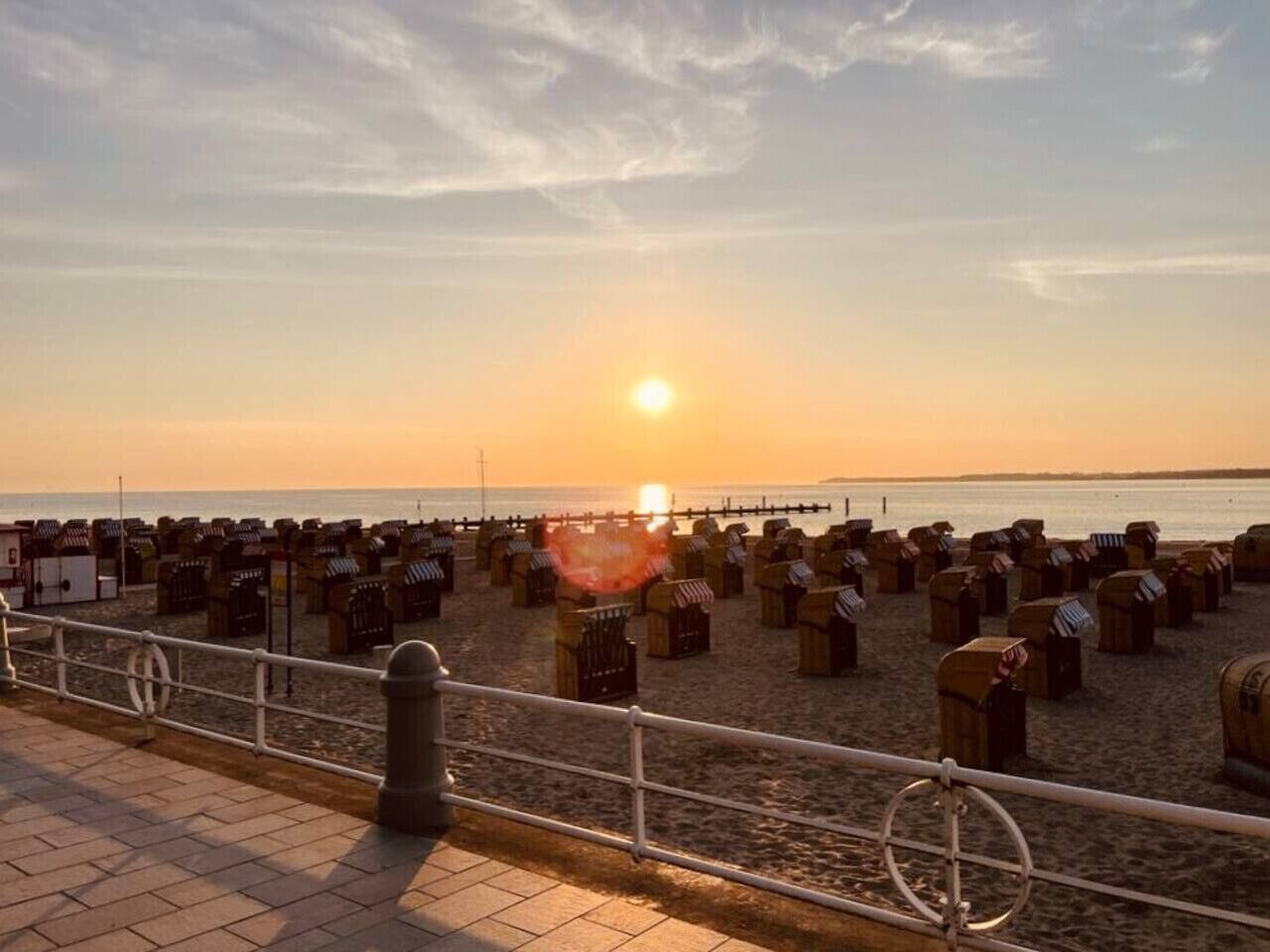 A beach with wooden structures, a railing, and a sunset in the background.