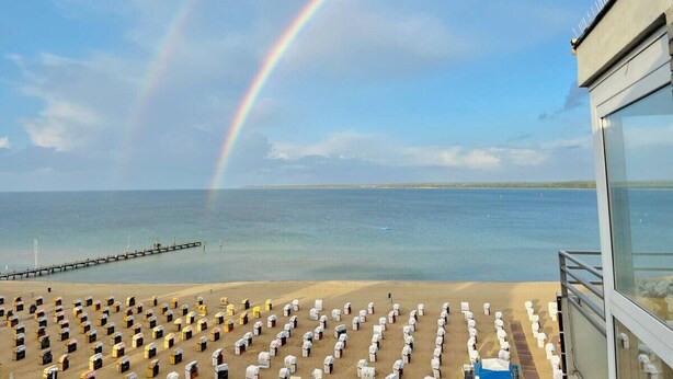 Ein Strand mit Reihen von Liegestühlen und ein Gebäude mit Glasfassade mit Blick aufs Meer.