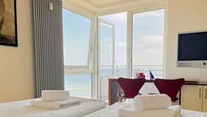 Ein Hotelzimmer mit zwei Betten, einem Fernseher, einem Schreibtisch mit Stuhl und Meerblick.