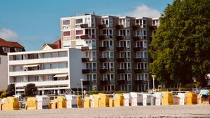 Ein mehrstöckiges Gebäude mit Balkonen, ein Strand im Vordergrund und ein klarer Himmel.