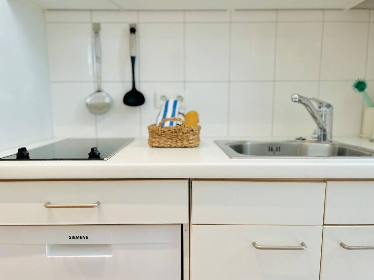 A kitchen with white cabinets, a Siemens brand refrigerator, a sink, and a hanging ladle.