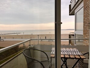 A balcony with a view of the beach, a table, and chairs.