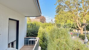 A balcony with a view of a garden and a cyclist in the distance.