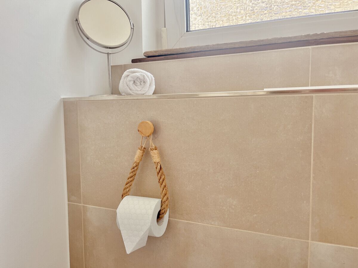 Un baño con azulejos color beige, un espejo redondo y un perchero con asa de cuerda.