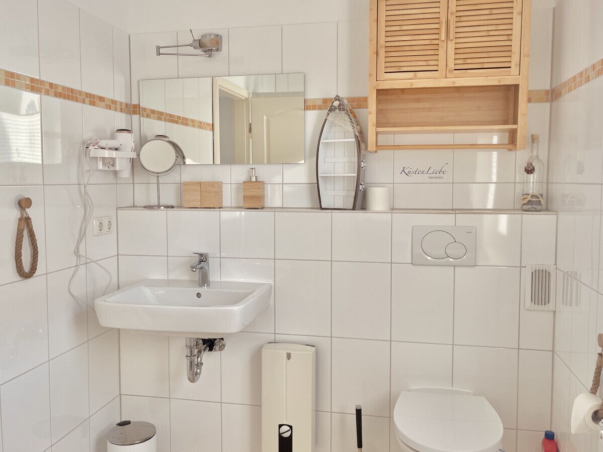 Un baño con lavamanos, espejo, inodoro y armario de madera.