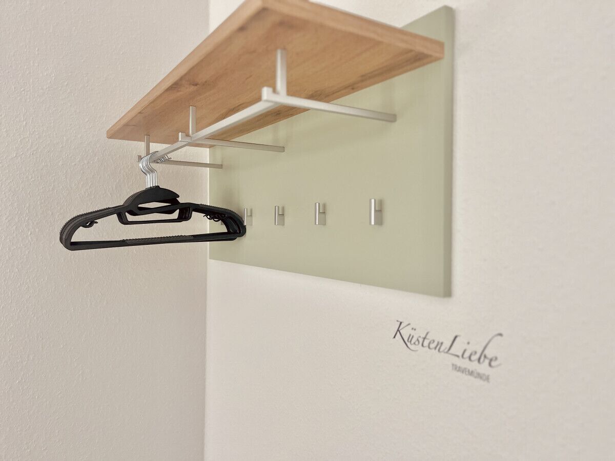 A wall-mounted coat rack with a wooden shelf above it.