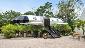 A futuristic, metallic structure with a staircase leading to a door, surrounded by palm trees and greenery. - Resort-Style Dome - Pool + Hot Tub + 5 Min to Beach (Potrero)