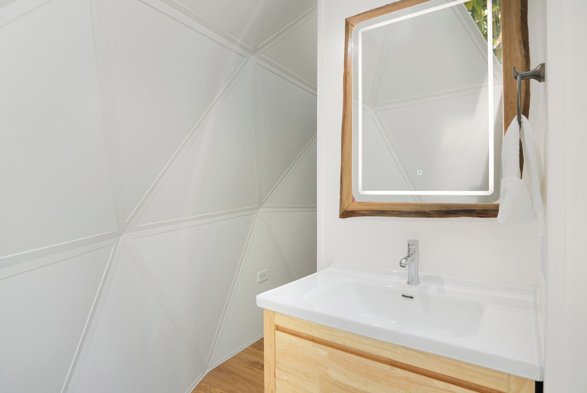 Une salle de bain avec des carreaux blancs, un meuble-lavabo en bois, un lavabo blanc et un miroir avec un cadre en bois.