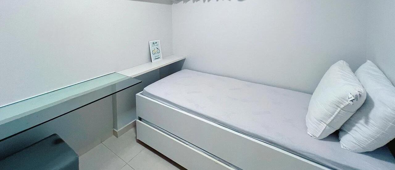 A small, compact bedroom with a single bed, a bedside table, and a nightstand.