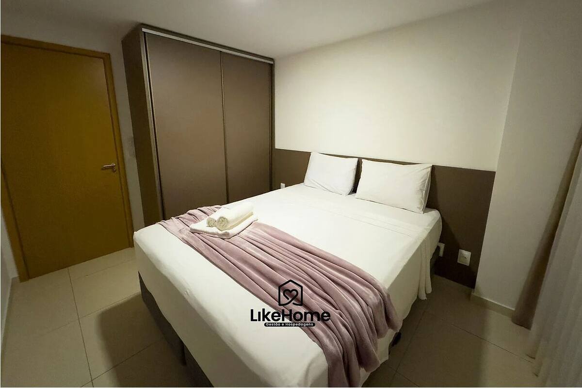 Una cama bien hecha con un edredón blanco y rosa, un armario marrón y una puerta blanca.
