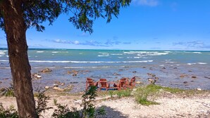 A beach with a table and chairs set up near the water, surrounded by rocks and vegetation.