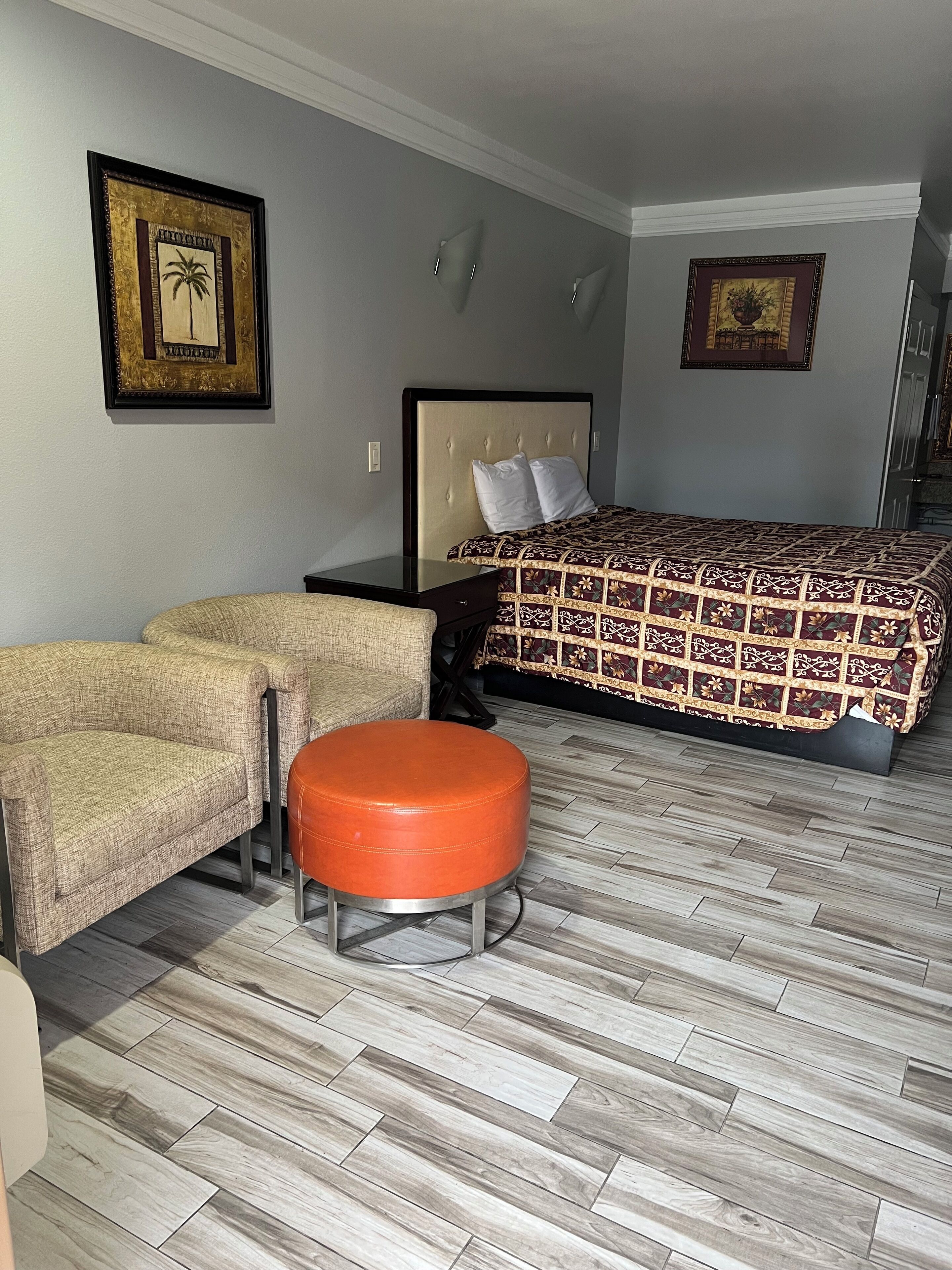 Una habitación de hotel con una cama, dos sofás, un reposapiés y suelo de madera.