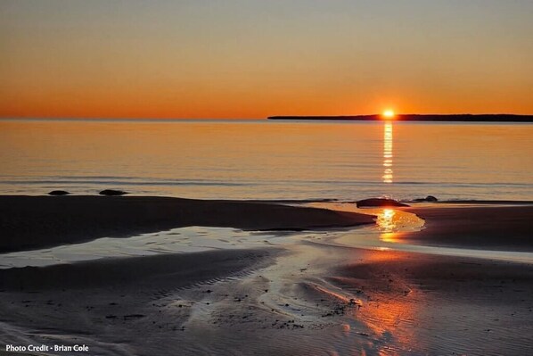 Ranta auringonlaskun aikaan, tyyni vesi heijastaa auringonvaloa.