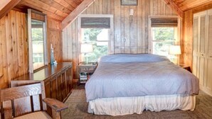 A bedroom with a wooden ceiling, a bed with a white and blue bedspread, a wooden nightstand, a chair, and a dresser. - Beaver Island - Cleveland's Big Chill  (Beaver Island)