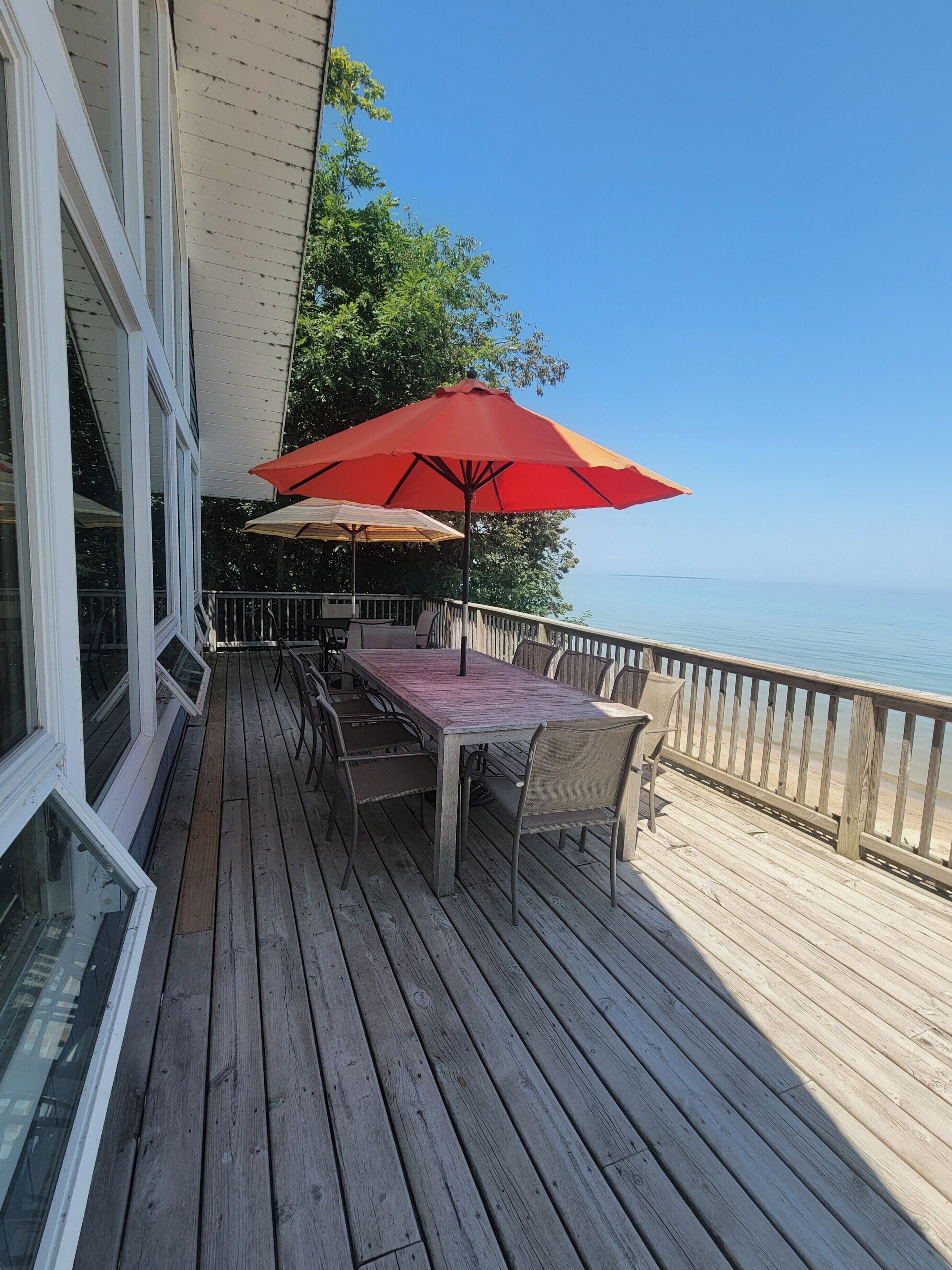 A wooden deck with a table and chairs, a red umbrella, and a view of the ocean.