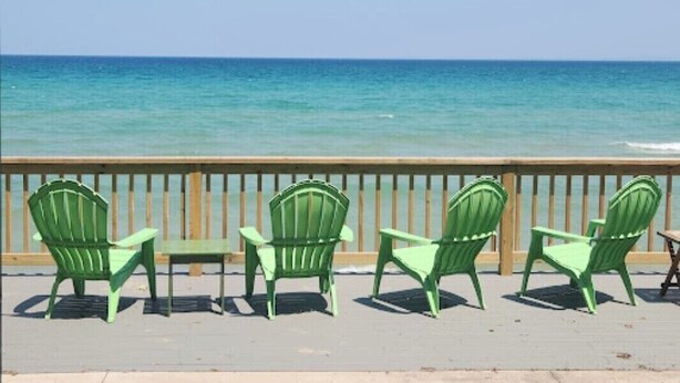 A wooden deck with green chairs and a table overlooking a calm sea. - Beaver Island - Cleveland's Big Chill  (Beaver Island)