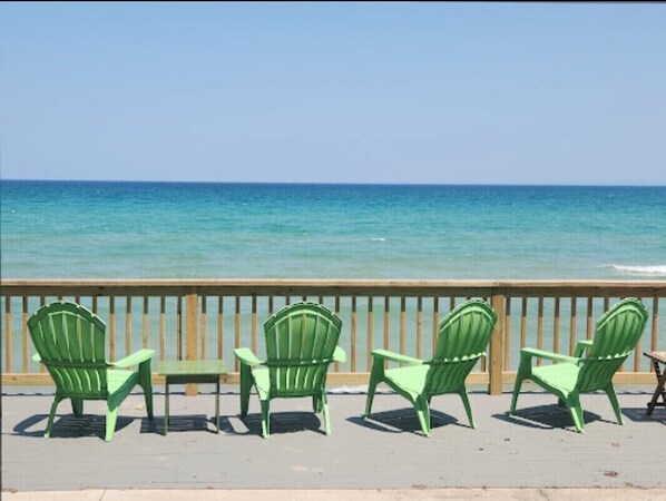 A wooden deck with green chairs and a table overlooking a calm sea.