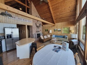 A cabin interior with a kitchen, dining area, and living room, featuring wooden walls and a high ceiling. - Beaver Island - Cleveland's Big Chill (Beaver Island)