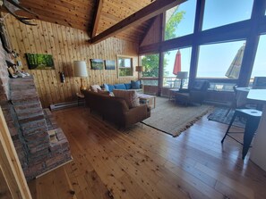 A spacious living area with a wooden floor, a brown sofa, a coffee table, and a large window offering a view of the outdoors. - Beaver Island - Cleveland's Big Chill (Beaver Island)