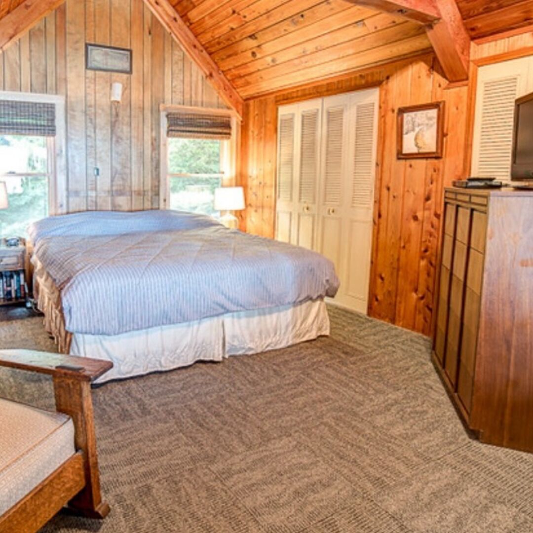 A wooden cabin bedroom with a large bed, a nightstand, a dresser, and a window with shutters.