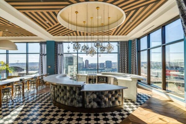 Enjoy a panoramic city view from the large window in this stylish room, featuring a circular bar area and geometric ceiling design.