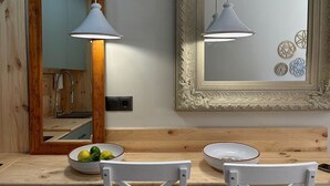Une table de salle à manger en bois, accompagnée de deux chaises blanches, d’un saladier rempli de fruits et d’un miroir décoratif doté d’un cadre orné.