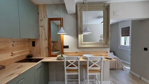 Une cuisine compacte avec des meubles en bois, un îlot central doté de deux tabourets de bar blancs et un grand miroir au-dessus de l’îlot.