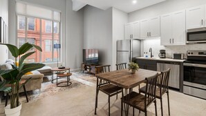 A modern kitchen with white cabinets, stainless steel appliances, and a dining area with a wooden table and chairs. - 2BR Near Fountain Sq.+ Carew Tower Deck | Downtown (Cincinnati)