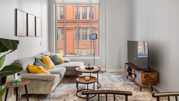 A modern living room with a sofa, coffee table, TV stand, and large window. - 2BR Near Fountain Sq.+ Carew Tower Deck | Downtown (Cincinnati)
