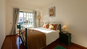 A bedroom with a bed, a nightstand, a lamp, a window with curtains, and a view of the outside.