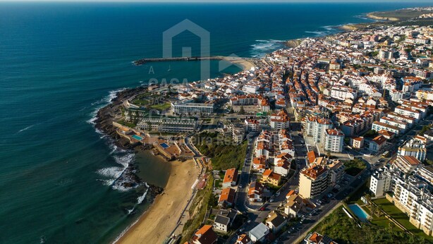 An aerial view of a coastal town with a beach, buildings, and a sea wall.