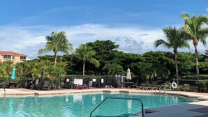 A swimming pool with lounge chairs and umbrellas, surrounded by palm trees and a clear blue sky. - Florida Vibes - A Fort Myers Gem- 2 Bedroom Condo.

 (Fort Myers)