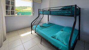 Una cama litera con ropa de cama color turquesa, una ventana con vistas a la vegetación y un suelo de baldosas.