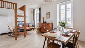 A modern living room with a wooden bunk bed, a dining table set for four, and a large window providing natural light. - Coquillages et Crustacés - Apt avec balcon vue mer (Saint-Malo)