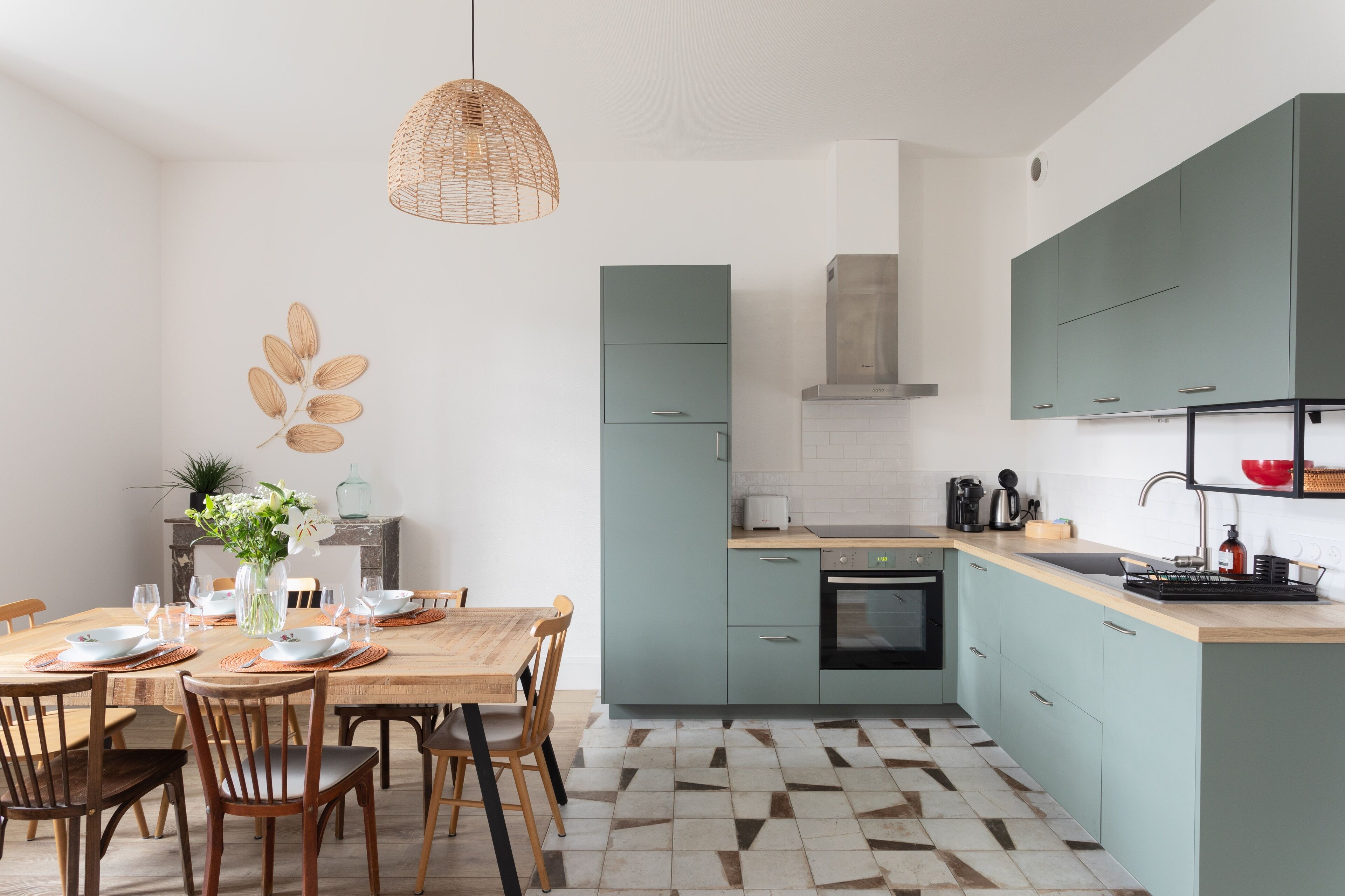 Une cuisine moderne avec des meubles de couleur turquoise, une table à manger en bois et un sol à motifs géométriques.