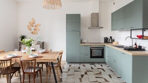 A modern kitchen with teal cabinets, a wooden dining table, and a geometric patterned floor. - Coquillages et Crustacés - Apt avec balcon vue mer (Saint-Malo)
